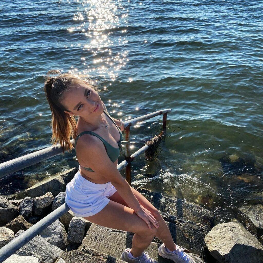 Shallon Olsen sits on a handrail while rocking a light green sports bra and white shorts.