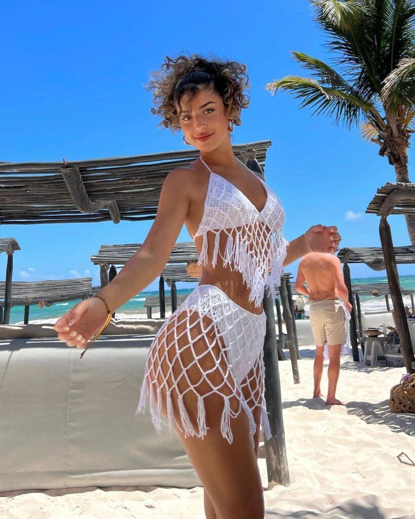 Zoe Gara wearing a white crochet bikini top with tassels and matching bottoms at the beach.