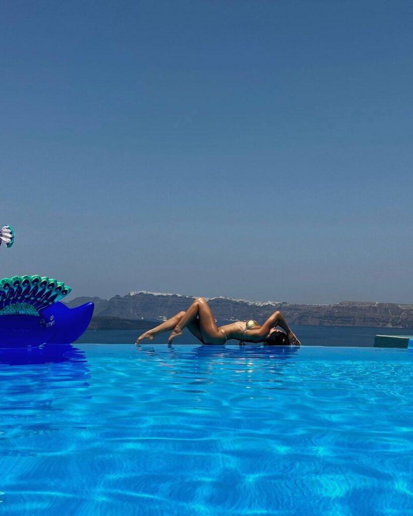 Andreea Dragoi lounges on the ledge of the pool while rocking a gold bikini.