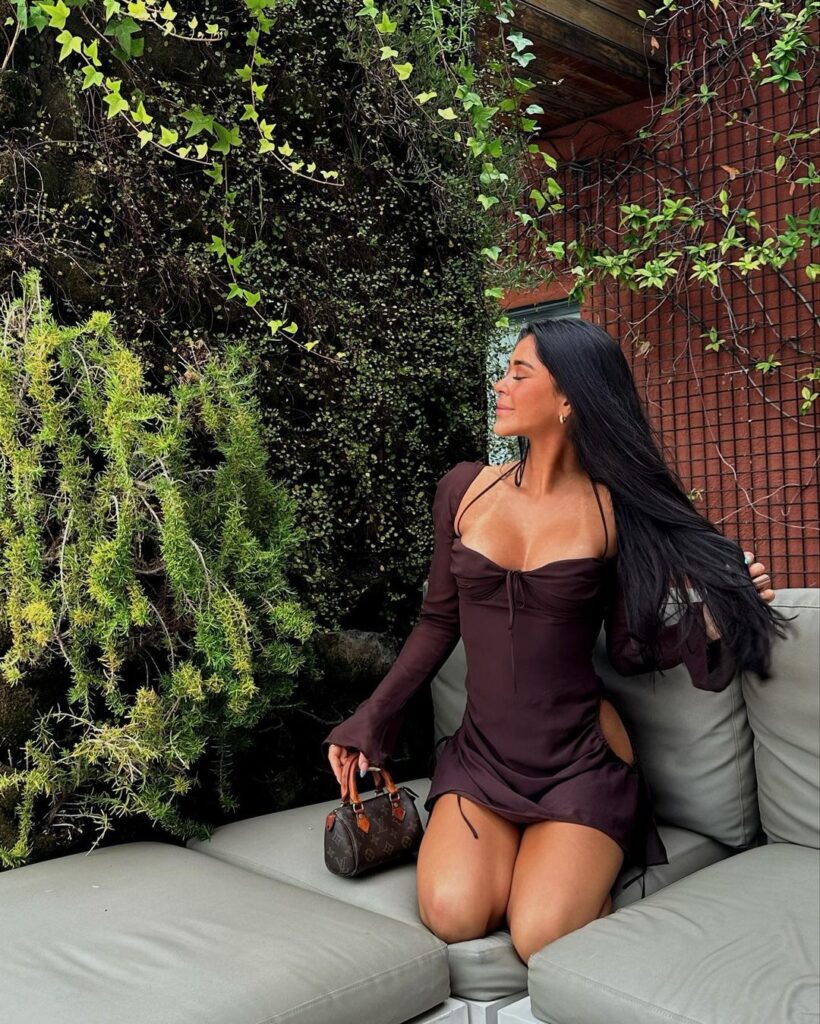 Mal Nicol kneels on a sun bed while wearing a skintight brown dress.