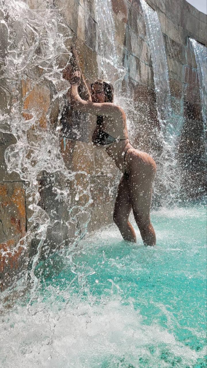 Dana Hamm in a bikini gets wet standing underneath a waterfall